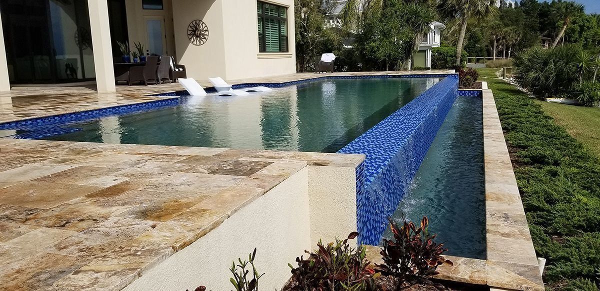 A rectangular pool with blue tile edging, next to a beige-colored patio.