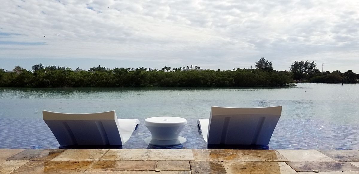 Two white lounge chairs and a small table face a tranquil lake.