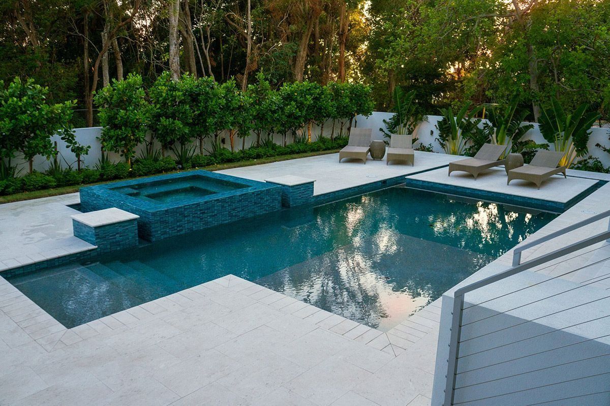 Swimming pool with hot tub, lounge chairs, and lush greenery in a backyard setting.