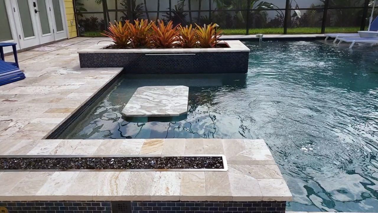 Swimming pool with built-in features: bar, seating, planter with orange plants, dark-tile accents.