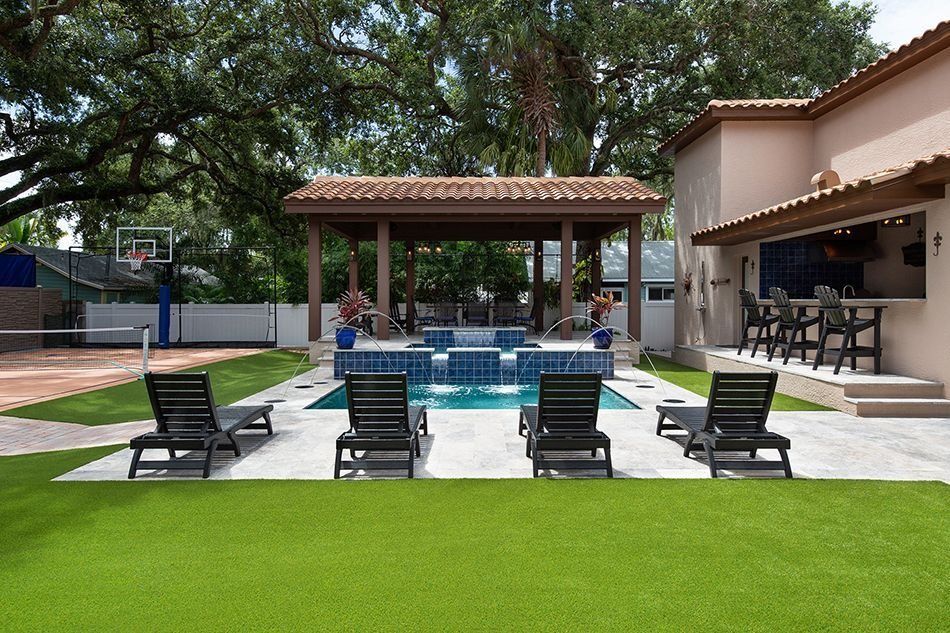 Backyard pool with a pergola, lounge chairs, and a bar attached to the house. Green grass surrounds.