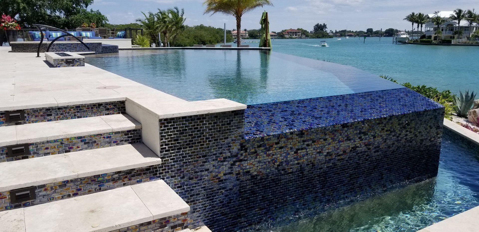 Infinity pool with blue-tiled wall overlooking the ocean and steps leading to the pool.
