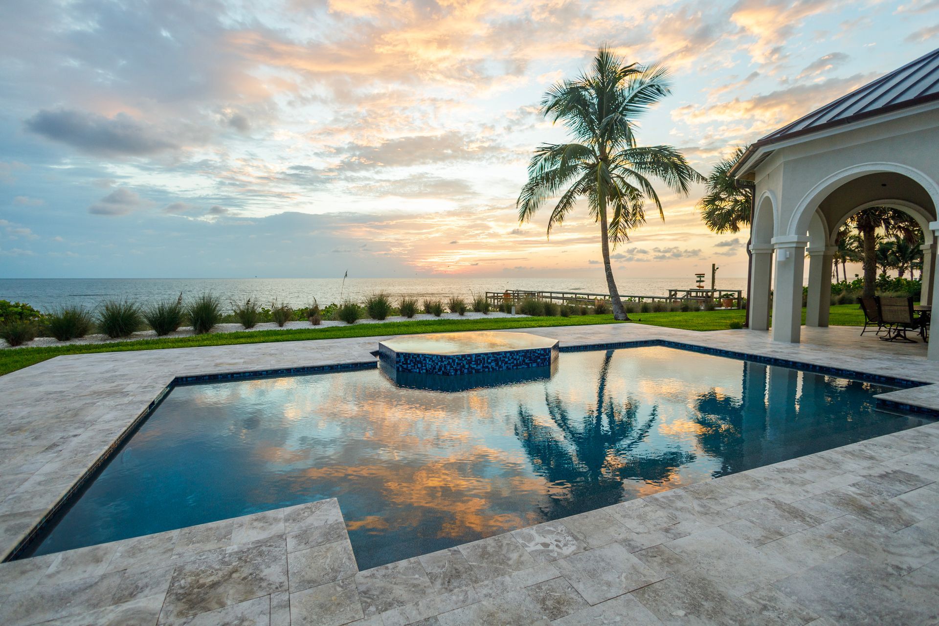 Pool overlooking ocean at sunset, palm tree, luxury home, reflective water.