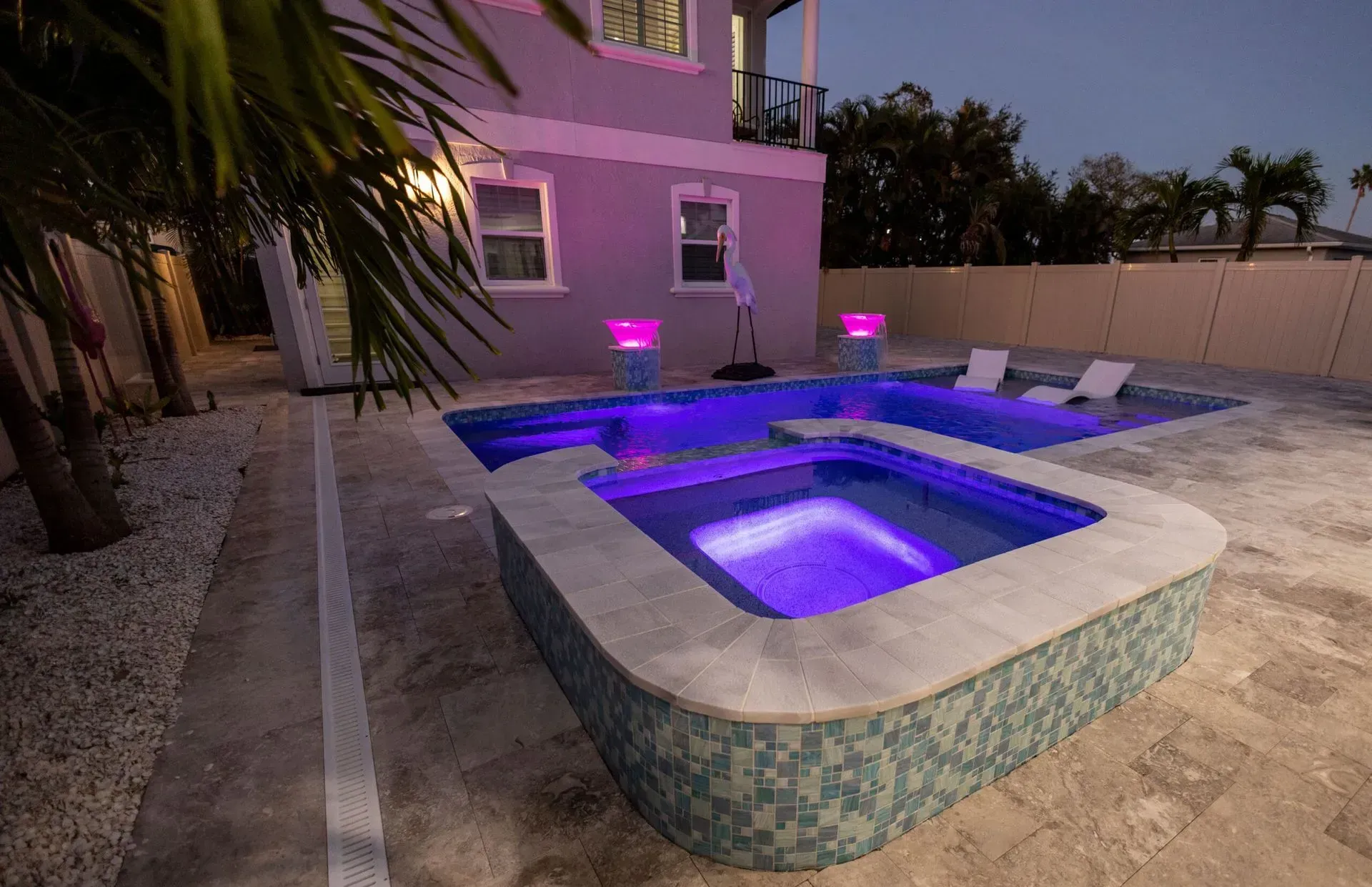 Backyard pool and spa lit with purple lights at dusk.