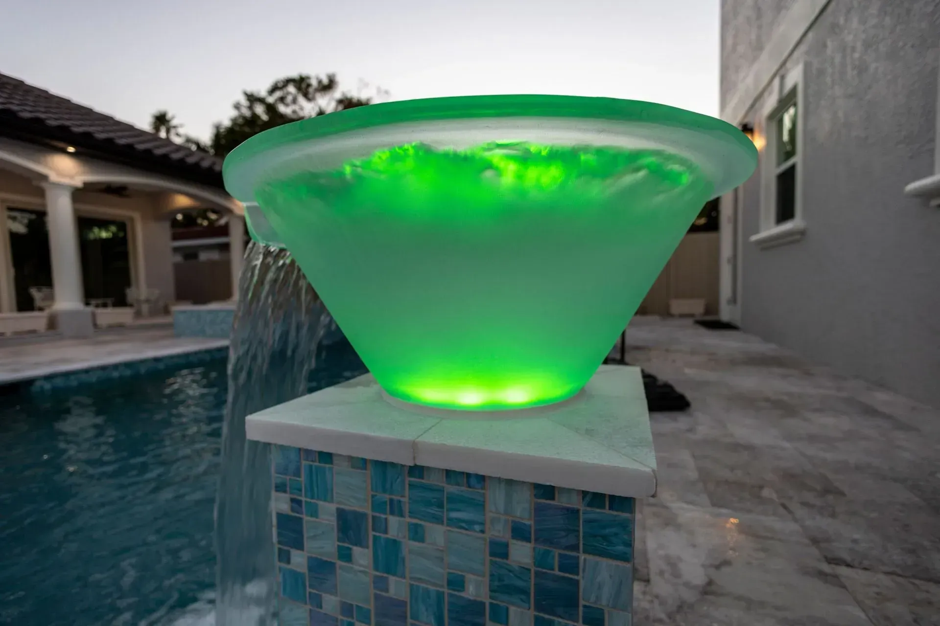 Green glowing fountain by a pool, outdoors.