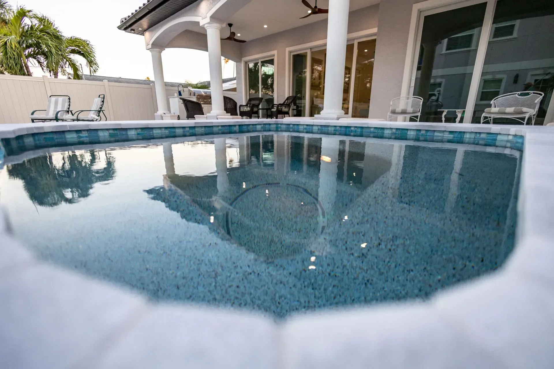Pool with a clear blue surface reflecting a white-columned patio and house.