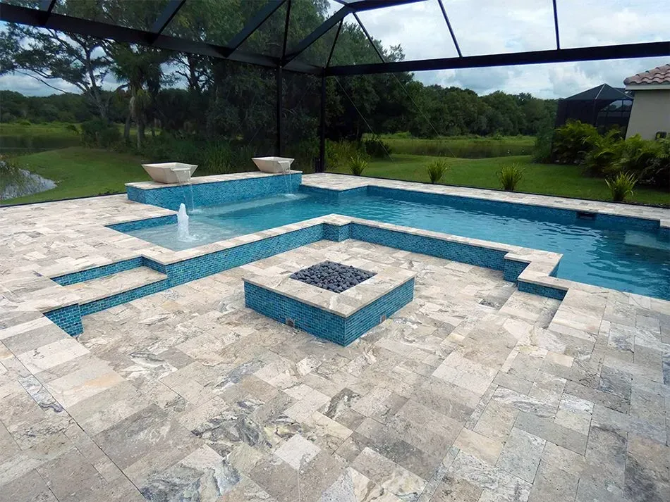 Pool and patio area with teal tiles, a water fountain, fire pit, and screen enclosure.