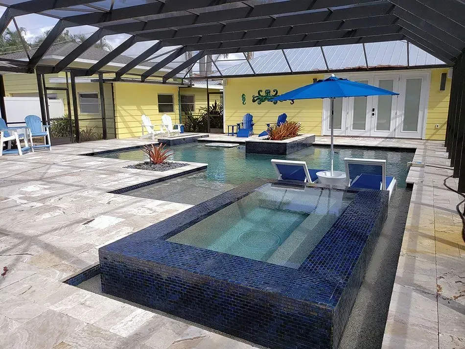 Swimming pool with blue tiled hot tub, chaise lounges, and blue umbrella in a backyard setting.