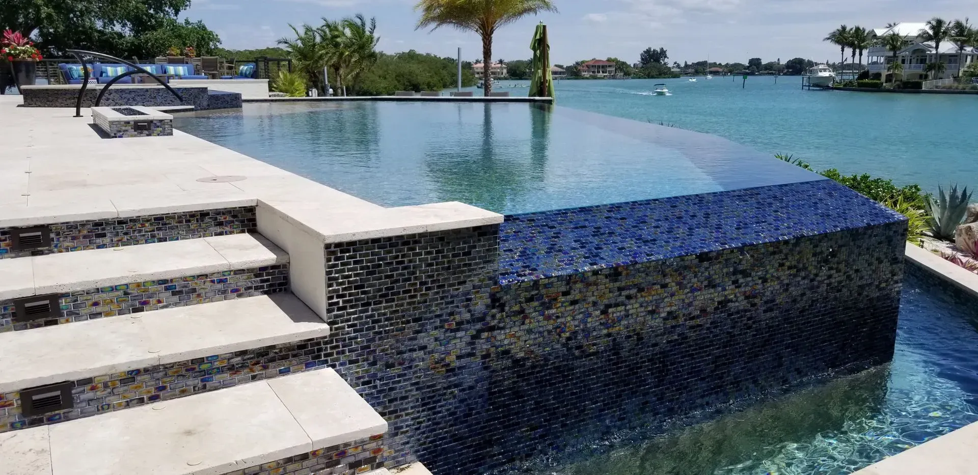 A pool with an infinity edge, steps, and a view of the water and buildings.