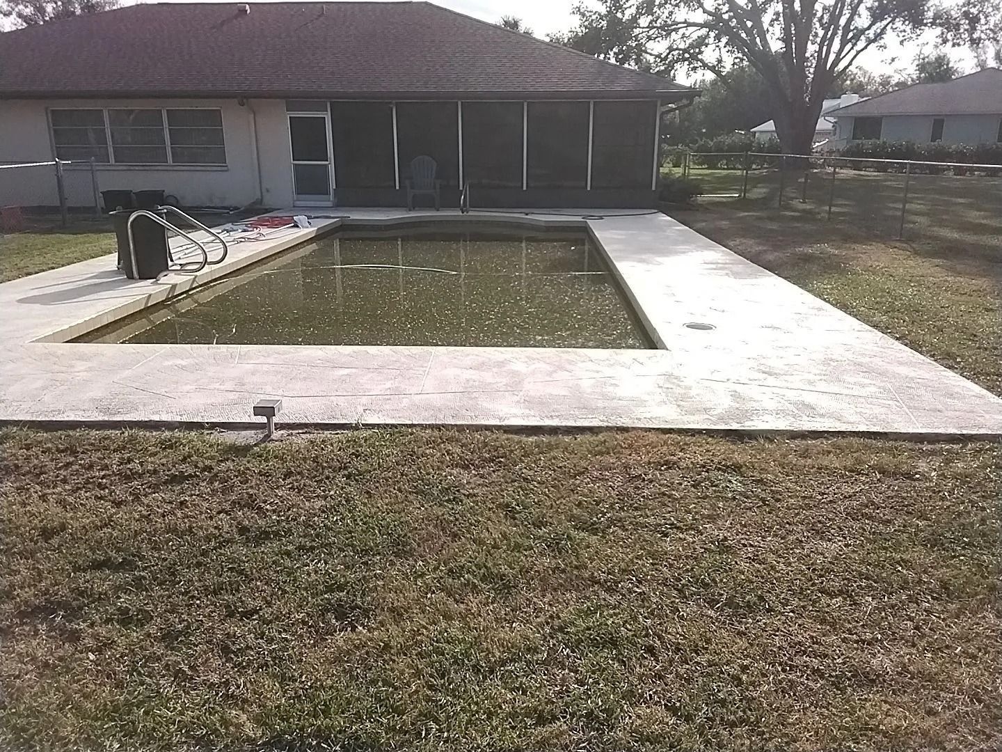 Backyard with a neglected, murky pool and concrete walkway; house and screen porch in the background.