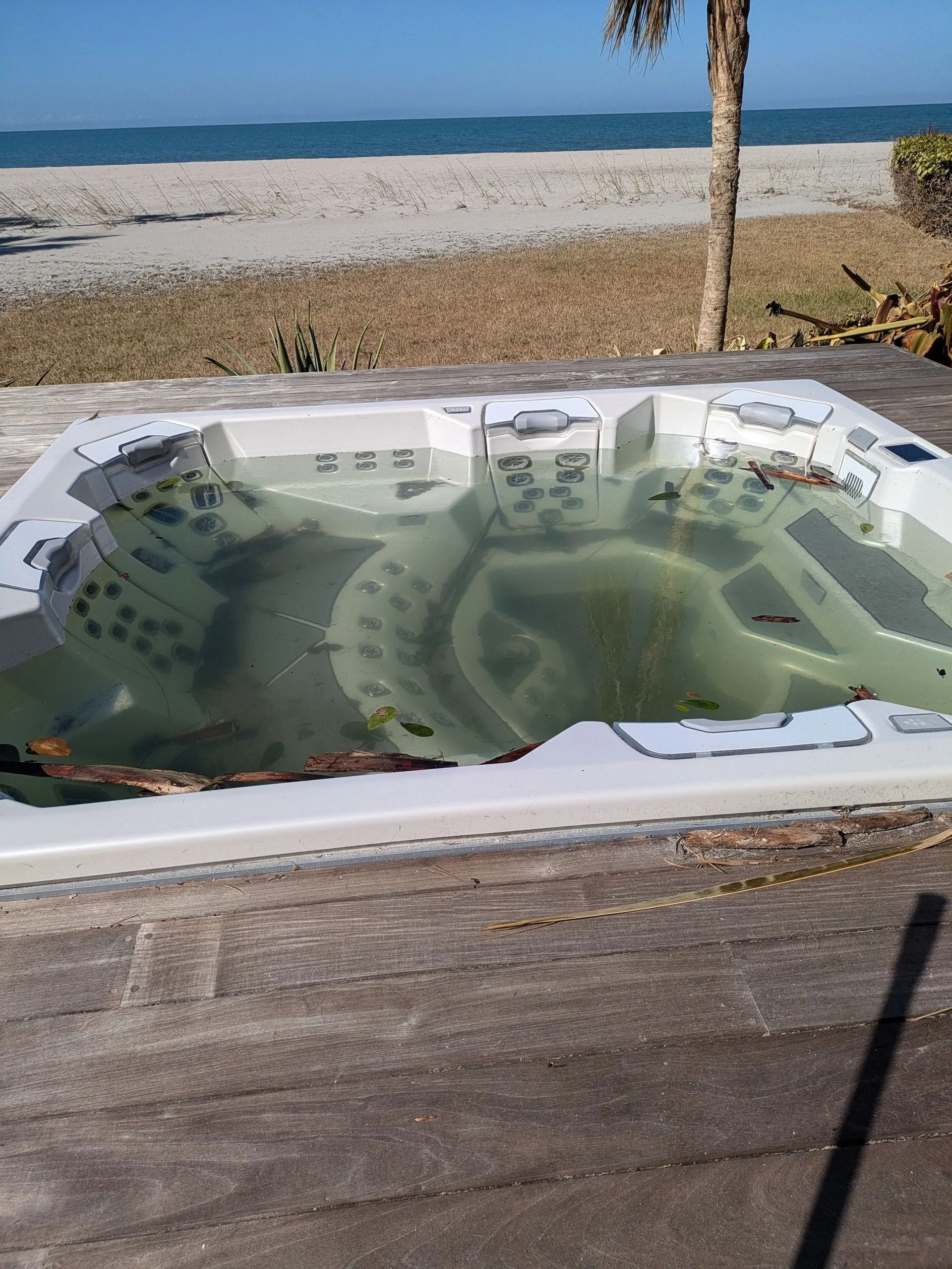Hot tub filled with murky water outdoors, beach in background.