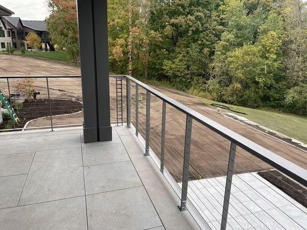 Balcony with gray tile floor and glass railing overlooking a wooded backyard and houses