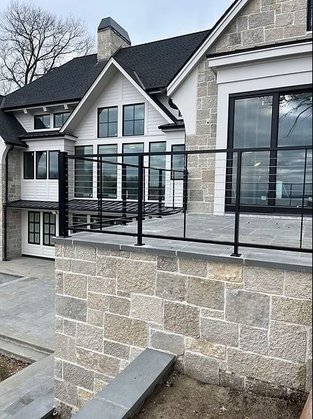 Modern house with large windows, black railing, and stone wall terrace outdoors