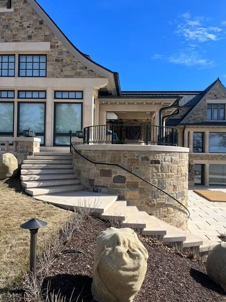 Stone mansion exterior with curved stairway, arched windows, and a lion statue in front under a blue sky