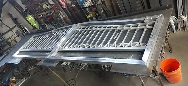 Long metal gate or grating leaning in a workshop, with a bright orange bucket nearby