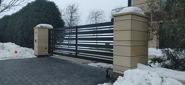Snow-lined metal gate with beige brick pillars at a driveway entrance