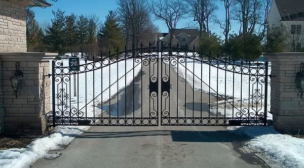 Closed black wrought-iron gate at a snow-lined driveway entrance on a sunny day