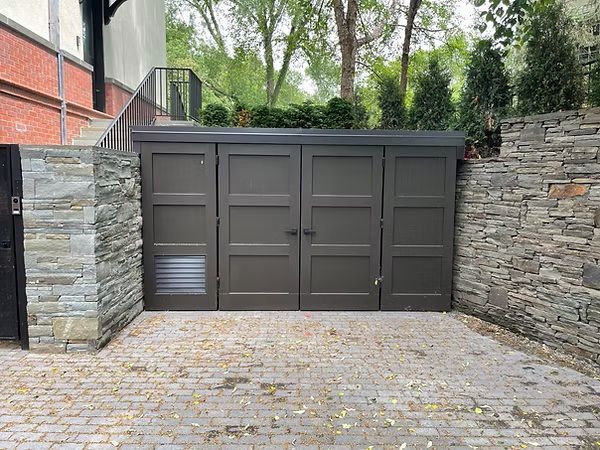 Gray double garage doors between stone walls and a paved driveway, with trees behind.