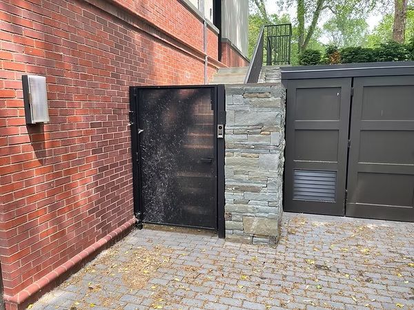 Brick courtyard with black metal gate, stone pillar, and dark gray garage doors