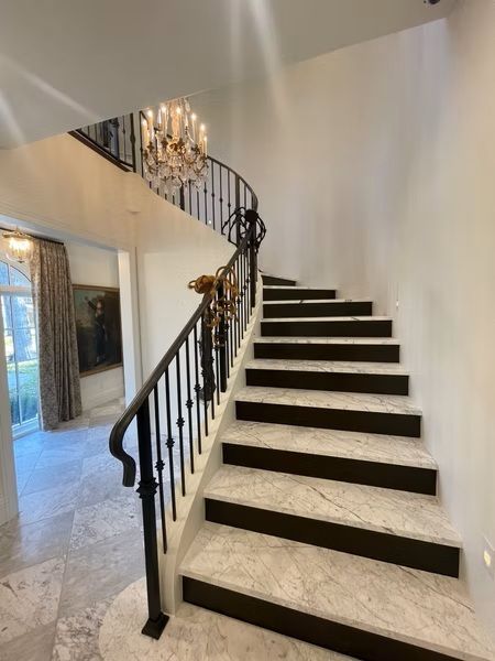 Elegant curved staircase with black railings and dark carpet runner in a bright foyer
