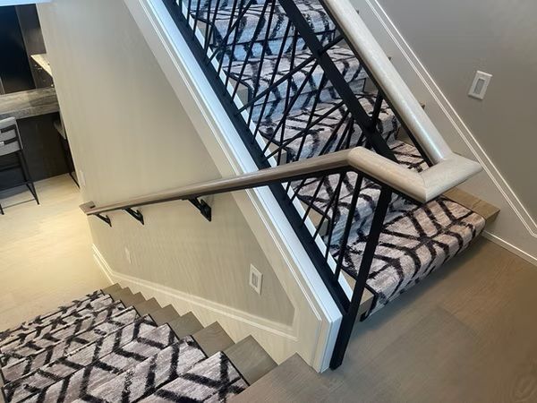 Stairwell with black handrails, patterned carpet, and a view down to a landing below