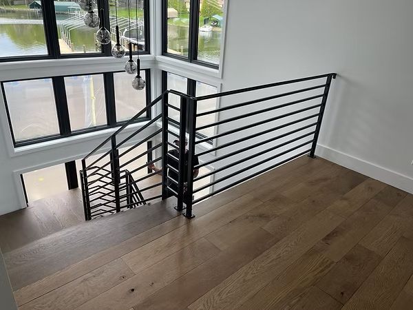 Modern stairwell with black metal railings, large windows, and wood flooring in a bright interior
