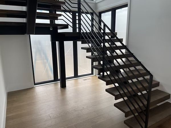 Modern interior with black metal staircase, wood steps, and large windows on a light wood floor