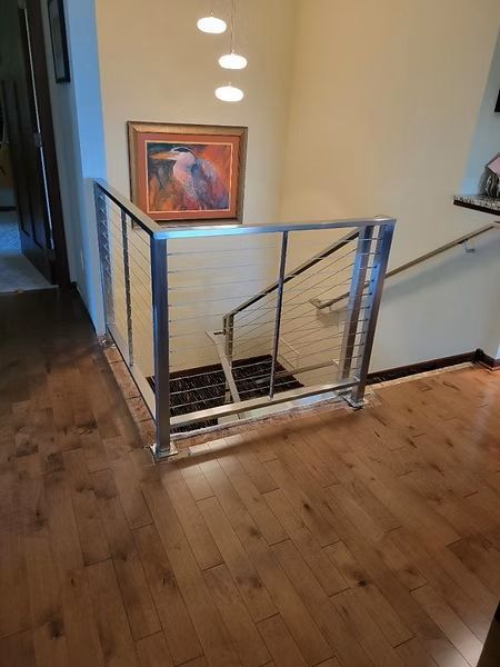Stair landing with a metal safety gate, wood floors, and framed artwork on the wall.