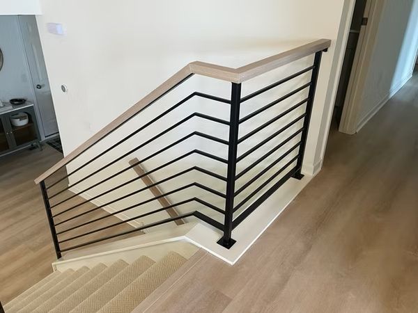 Modern black metal stair railing with horizontal cables in a light wood-floored hallway