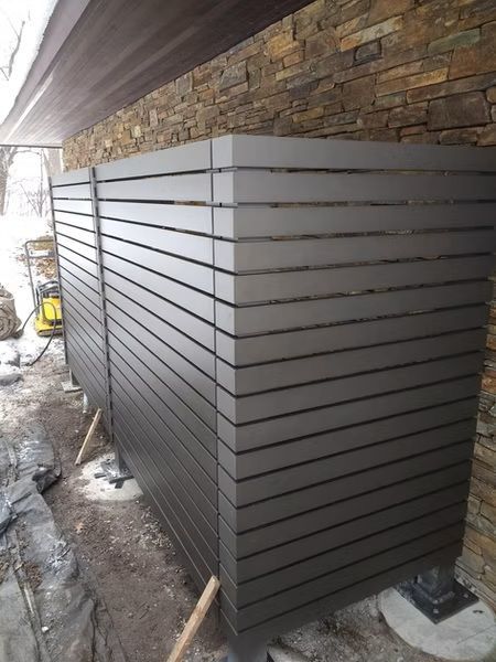 Dark gray slatted enclosure beside a stone wall under a covered outdoor area