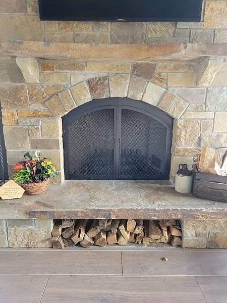 Stone fireplace with black mesh doors, wood storage below, and flowers on the hearth
