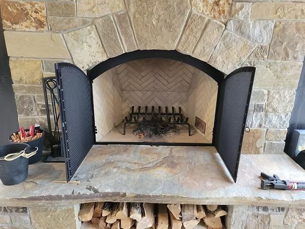 Stone fireplace with open black doors and stacked firewood underneath