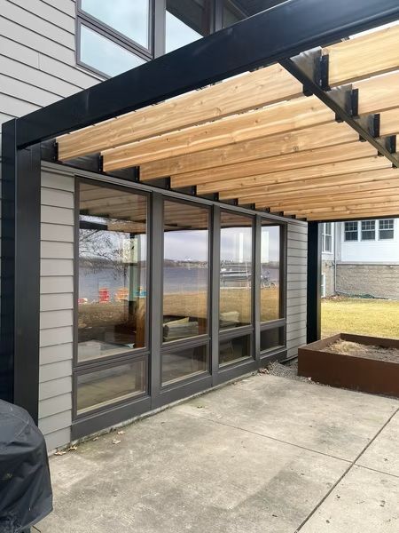 Covered patio with glass doors, wood pergola ceiling, and concrete courtyard beside a building.