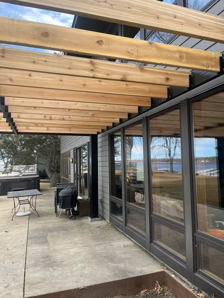 Covered patio with wooden beams, glass doors, concrete floor, and outdoor table and chairs overlooking water