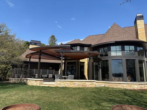 Large brick house with covered patio, arched windows, and a grassy backyard under a blue sky