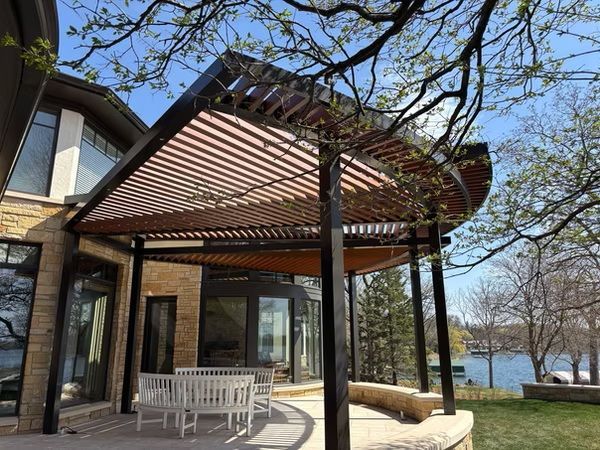 Patio with wooden pergola beside a lakeside house, white table, and leafless trees