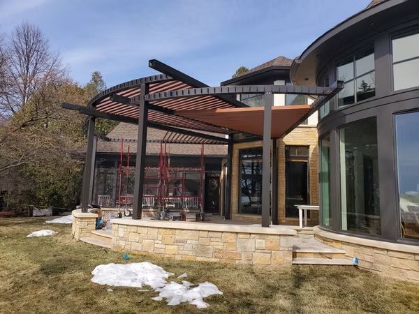 Stone patio beside modern house with pergola and glass sunroom, patchy snow on the ground.