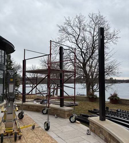 Scaffolding beside a lakeside walkway under a cloudy sky, with a leafless tree and equipment carts.