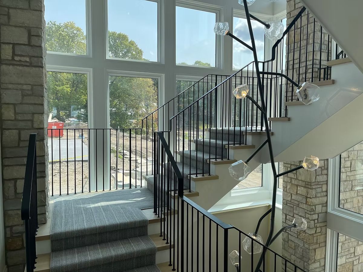 Interior staircase with black railings, gray carpeted steps, and large windows overlooking outdoors