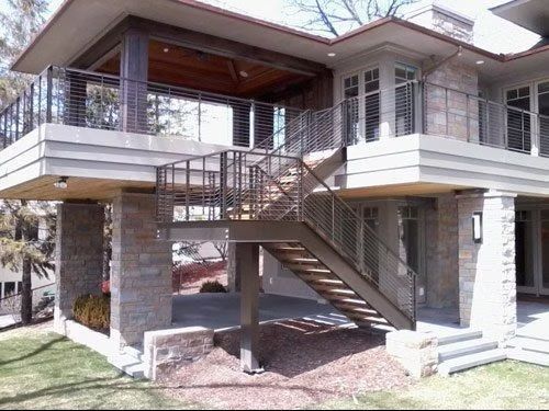 Modern elevated house with exterior stairs, stone pillars, and a covered balcony
