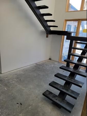 Modern black metal staircase in a bright unfinished room with concrete floor and large windows