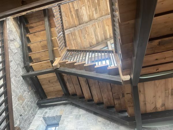Wooden spiral staircase under a rustic thatched roof with stone walls below