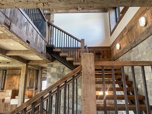 Wood-paneled rustic stairwell with exposed beams, railings, and wall sconces in a lodge-style interior