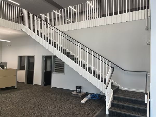 Office lobby with white staircase and railing, gray carpet, and open doorways