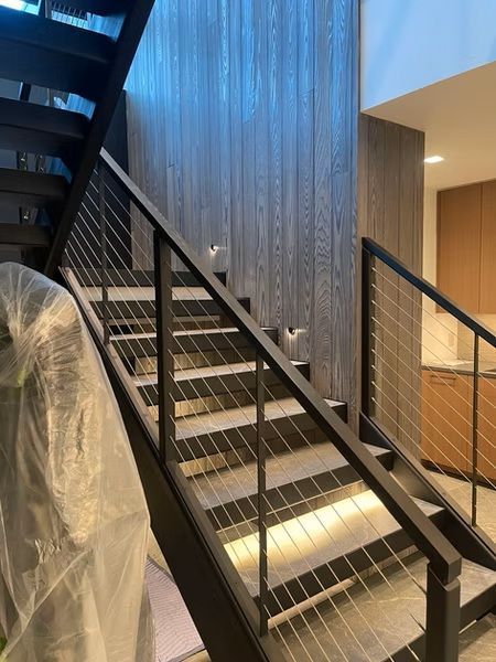 Indoor staircase with black railings, wood-paneled wall, and warm accent lighting beneath the steps