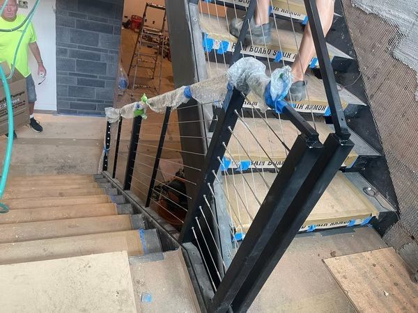 Worker on a staircase landing, installing black metal railings beside a concrete stairwell.