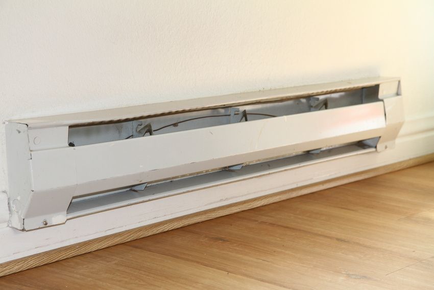 Damaged white baseboard heater with a bent front cover against a wall and wood floor