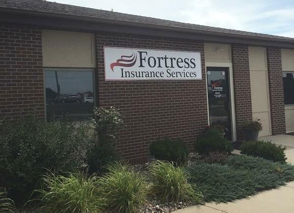 Fortress Insurance Services storefront with sign on brick building, surrounded by plants.