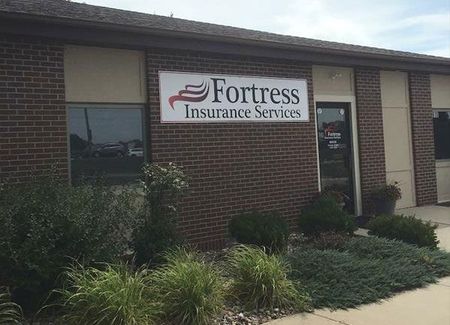 Fortress Insurance Services storefront with sign on brick building, surrounded by plants.