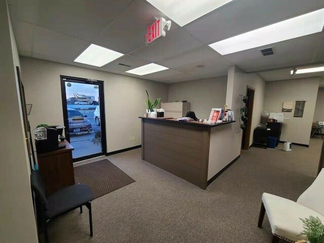 Office reception area, desk with a computer and plants. Glass door to the outside.